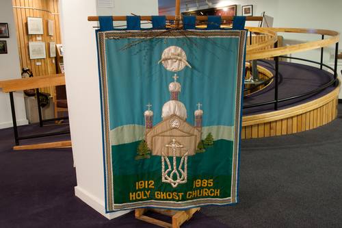 This processional banner was made by parishioners in 1985. Their names are embroidered on the bottom corner: Betty Marmulak, Mary Pronko, Kaye Melenchuk, Lydia Tatanish, Helen MacLean. It was donated to the Holy Ghost parish in memory of Walter Marmulak, by his family. In the entrance to the Holy Ghost Ukrainian Catholic Church, a table is laid with prayer books, church bulletins and other items.