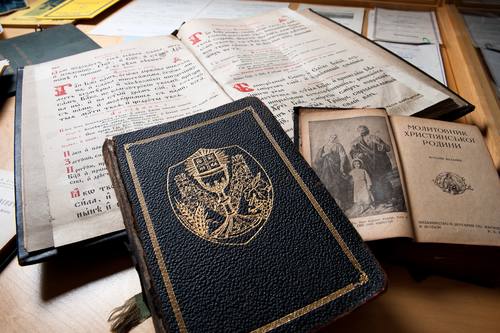 These are historical prayer books of the Holy Ghost Ukrainian Catholic Church.

The priest’s servicebook that lies open is from the early 1900s, and is in the old Church Slavonic language.

The “Prayerbook for the Christian Family,” open to an icon of the Holy Family, was printed in the city of Zhovkva (present-day Ukraine), in 1936.

The closed book, embossed with a Chalice on the cover, was printed in Philadelphia in 1954. It is the Divine Liturgy of St. John Chrysostom – regularly prayed, like the Roman Catholic Mass.